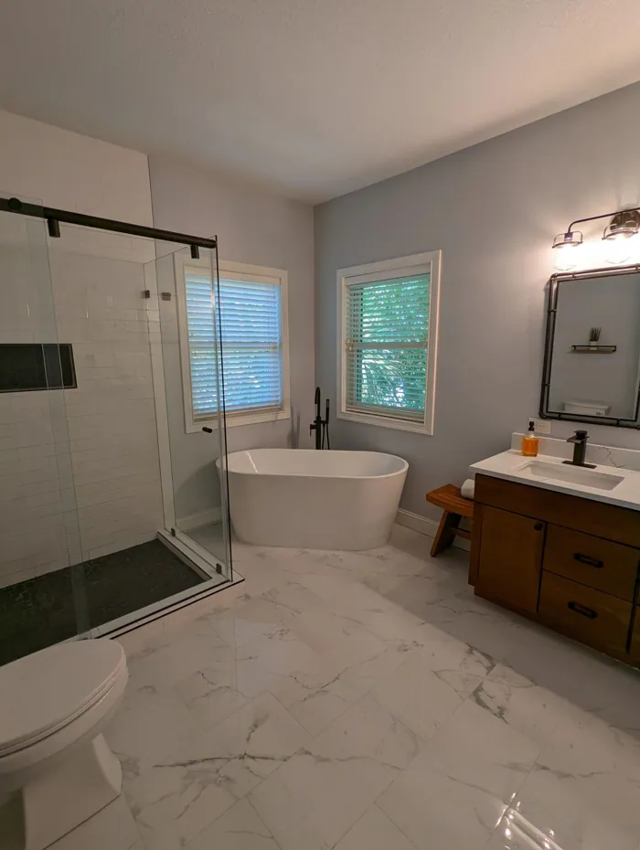 Bathroom with freestanding soaking tub, frameless glass shower, marble-look floor tile and wood vanity.