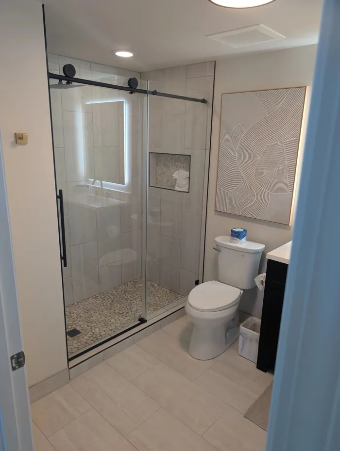 Bathroom with frameless glass shower, pebble shower floor and backlit mirror.
