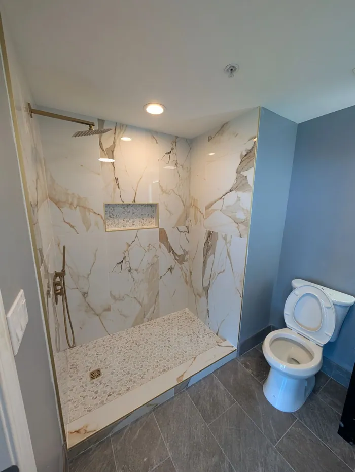 Walk-in shower finished in gold-veined marble slab with brass rain head and mosaic floor.