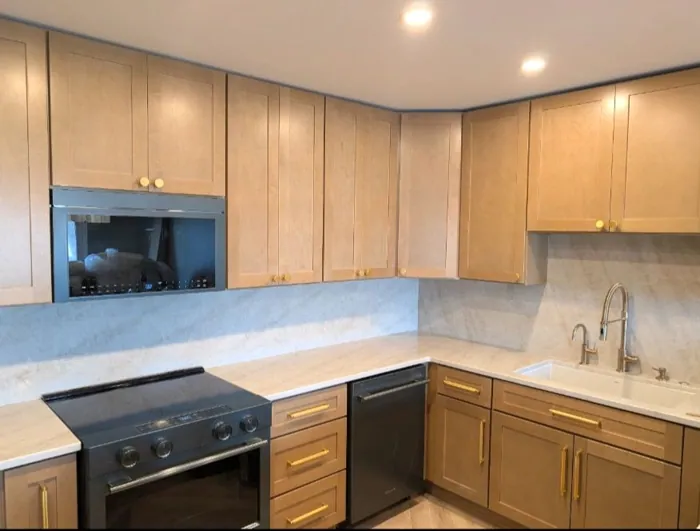 Kitchen with light maple cabinetry, light stone counters and brass hardware.