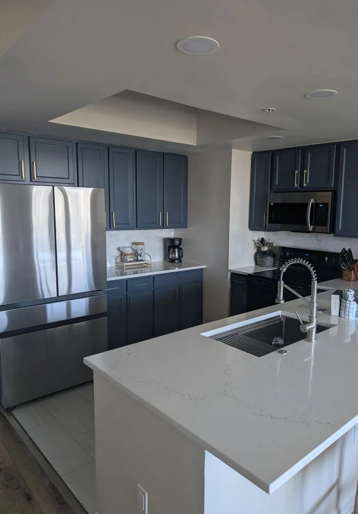 Kitchen with navy cabinetry, quartz waterfall island, marble hex backsplash and stainless appliances.