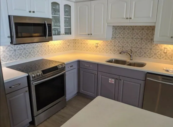 Kitchen with two-tone white and grey cabinetry and patterned tile backsplash.