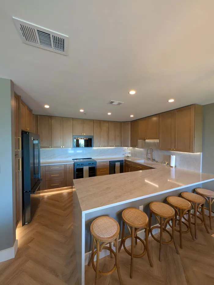 Kitchen with stone waterfall peninsula, stained shaker cabinetry, brass hardware, herringbone flooring and rattan stools.